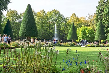 residenzgarten-wuerzburg.jpg Menschen spazieren in einem gepflegten Garten mit Springbrunnen und Bäumen.
