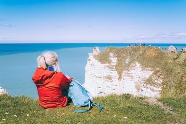 Person in roter Jacke sitzt auf einer Klippe mit Blick auf das Meer.