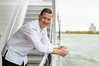 Mann in weissem Hemd lehnt am Geländer eines Bootes.