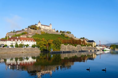 Festung auf Hügel am Flussufer mit Enten im Wasser.