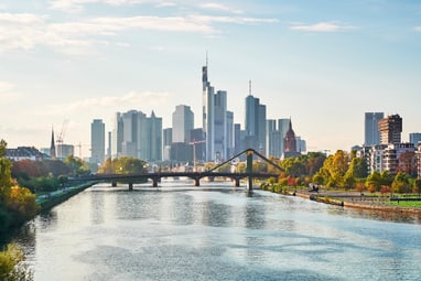 frankfurt-skyline-trifft-mainufer.jpg Skyline von Wolkenkratzern hinter Fluss und Brücke bei Tageslicht.