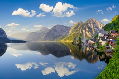 Bergdorf am ruhigen See mit Spiegelung und Bergen im Hintergrund.