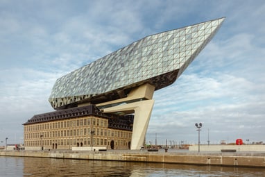 Modernes Gebäude mit schiffsförmiger Spitze über historischem Backsteingebäude am Wasser.