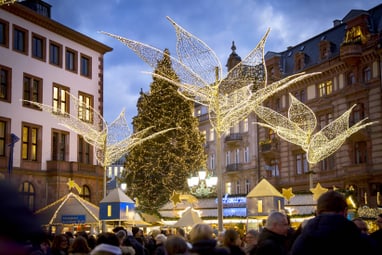 Weihnachtsmarkt mit Lichtdekorationen und grossen Gebäuden im Hintergrund.