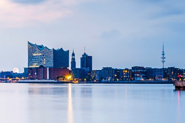 Stadtsilhouette bei Dämmerung mit Wasser im Vordergrund.