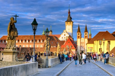 Menschen auf mittelalterlicher Brücke mit Kirche im Hintergrund.