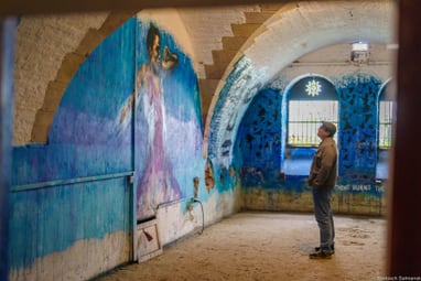 ein-geheimnisvoller-hoehlenartiger-ort-der-graffiti-kunst-ma.jpg Mann betrachtet Wandgemälde in blauem Raum.