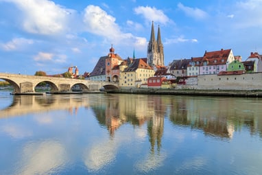 Flussblick auf mittelalterliche Stadt mit Brücke und Kirchtürmen.