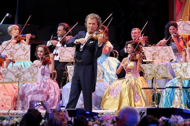 Geiger spielt mit Orchester auf Bühne in festlichen Kleidern.