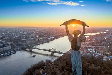 Monument über Budapest bei Sonnenuntergang mit Fluss und Brücke.