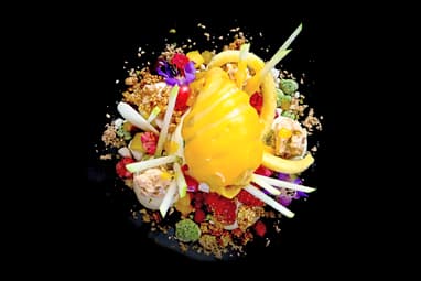 Gourmet-Dessert mit bunten Früchten und Dekoration auf schwarzem Teller.