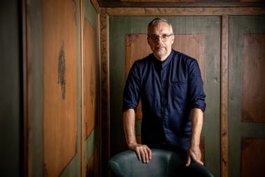 Mann in blauem Hemd steht in holzgetäfeltem Raum.