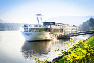 Flusskreuzfahrtschiff auf ruhigem Fluss bei sonnigem Wetter.