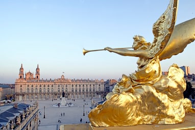 Goldene Statue mit Trompete auf Balkon mit Blick über grossen Platz und historische Gebäude.