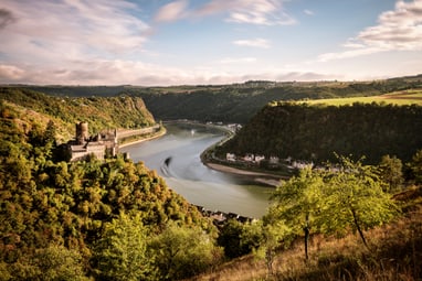 mittelrheintal.jpg Burgruine am Fluss mit bewaldeten Hügeln im Hintergrund.