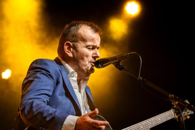 Mann in blauem Anzug spielt Gitarre auf der Bühne.