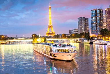 Beleuchtetes Schiff auf der Seine vor Eiffelturm bei Abenddämmerung.