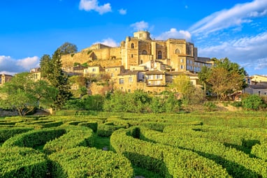 dorf-grignan.jpg Historische Burg auf einem Hügel mit Labyrinth aus Hecken im Vordergrund.