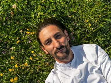 das-excellence-gourmetfestival-10.jpg Mann in weissem Hemd liegt auf Wiese mit Blumen.