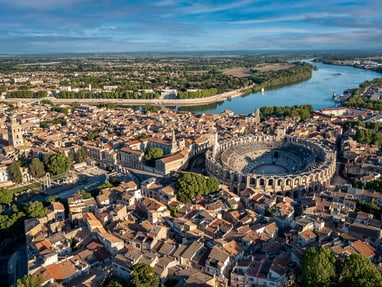 arles-von-den-roemern-gepraegt-von-vincent-van-gogh-geliebt.jpg Luftaufnahme einer Stadt mit antikem Amphitheater und Fluss.