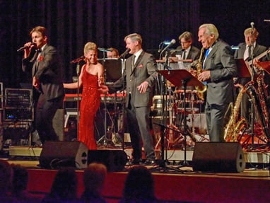pepe-lienhard-und-orchester-musik-tanz-und-pure-lebensfreude.jpg Band auf der Bühne mit Sängern und Musikern in formeller Kleidung.