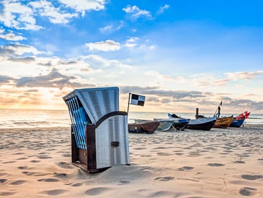 strandkorb-an-der-ostseekueste.jpg Sonnenuntergang am Strand mit Strandkorb und Fischerbooten.
