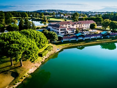 golf-grand-avignon-wurde-vom-architekten-georges-roumeas-mit.jpg Luftaufnahme eines Gebäudes am See mit Bäumen und Landschaft.