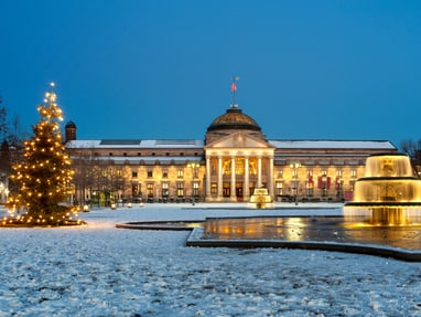 wiesbaden.jpg Beleuchtetes historisches Gebäude und Brunnen bei Schnee und Weihnachtsbaum.