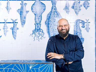 Mann im dunklen Hemd steht vor einer blauen Fliesenwand mit Fischmotiven.