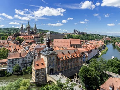 Stadtansicht mit Fluss und historischen Gebäuden vor blauem Himmel.