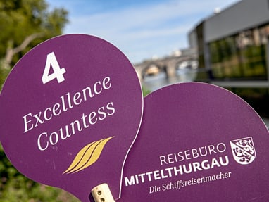 Zwei lila Schilder mit Aufschrift 'Excellence Countess' und 'Reisebüro Mittelthurgau', im Freien.