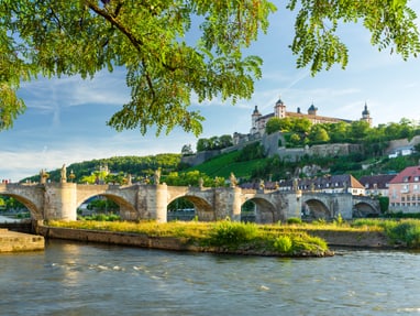 hoch-ueber-wuerzburg-thront-die-festung-marienberg.jpg Alte Steinbrücke über Fluss mit Festung im Hintergrund.