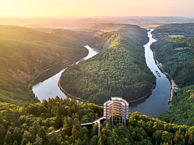 die-saarschleife-zeigt-die-naturwunder-im-naturpark-saar-hun.jpg Luftaufnahme einer Flussbiegung im bewaldeten Tal bei Sonnenuntergang.