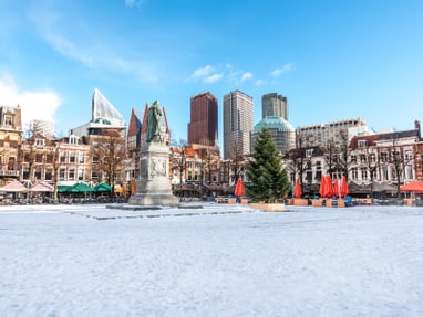 den-haag.jpg Schneebedeckter Platz mit Statue und Hochhäusern im Hintergrund.