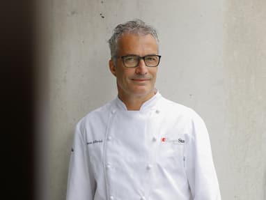 das-excellence-gourmetfestival-10.jpg Mann in weissem Kochmantel steht vor einer Betonwand.