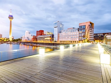 twerenbold_73386.jpg Holzsteg und beleuchtete Skyline am Abend in Düsseldorf.