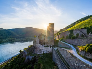 die-burgruine-ehrenfels-markiert-den-eingang-zum-unesco-welt.jpg Burgruine am Fluss mit Weinbergen im Sonnenuntergang.