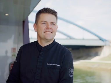 stefan-heilemann.jpg Person in dunkler Uniform lächelt an Bord eines Schiffes mit einer Brücke im Hintergrund.