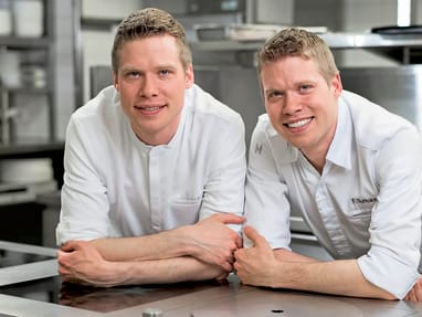 das-excellence-gourmetfestival-4.jpg Zwei Männer in weissen Kochjacken lächeln in einer professionellen Küche.