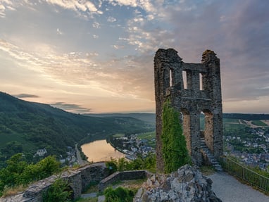 die-hoehenburgruine-grevenburg-mit-blick-ueber-die-moselschl.jpg Ruine mit Aussicht auf Fluss und Landschaft bei Sonnenuntergang.