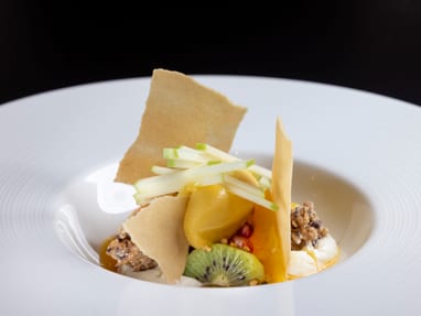 Elegantes Dessert mit Obst und knusprigen Stücken auf einem weissen Teller.