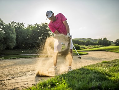 golfclub-botaniq.jpg Golfer im rosa Hemd schlägt aus einem Sandbunker.
