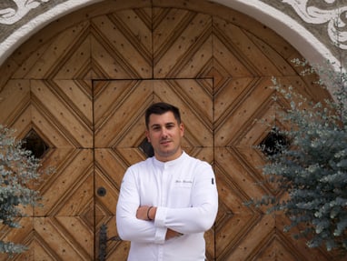 das-excellence-gourmetfestival-10.jpg Mann in weissem Hemd steht vor dekorativer Holztür.