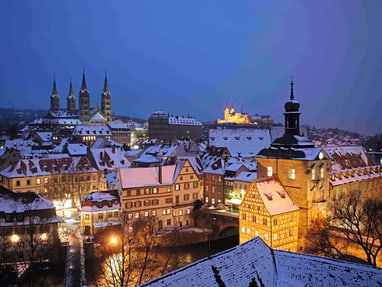 bamberg.jpg Verschneite Stadtansicht mit beleuchteten historischen Gebäuden bei Dämmerung.