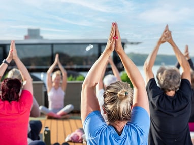 Menschen, die im Freien Yoga machen, mit den Armen über dem Kopf.