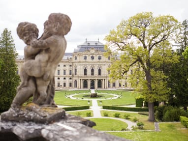 twerenbold_101989.jpg Steinfigur vor barockem Schloss mit Garten.