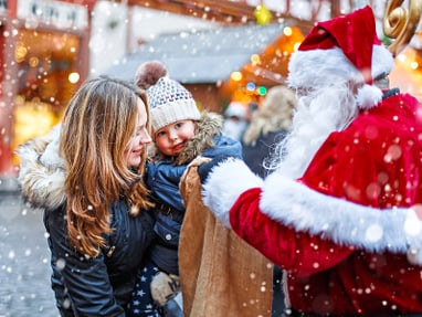 .jpg Kind und Frau treffen Weihnachtsmann auf verschneitem Weihnachtsmarkt.