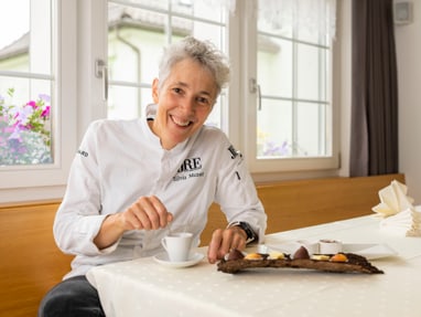 das-excellence-gourmetfestival-10.jpg Frau in weisser Kochjacke sitzt am Tisch mit Kaffee und Dessert.