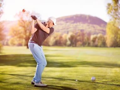 Person beim Golfschwung auf einem Golfplatz vor Bergkulisse.