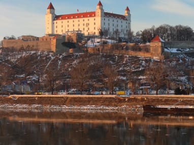 aussicht-auf-die-burg-von-bratislava.jpg Burg auf Hügel mit Fluss und Bäumen im Vordergrund.